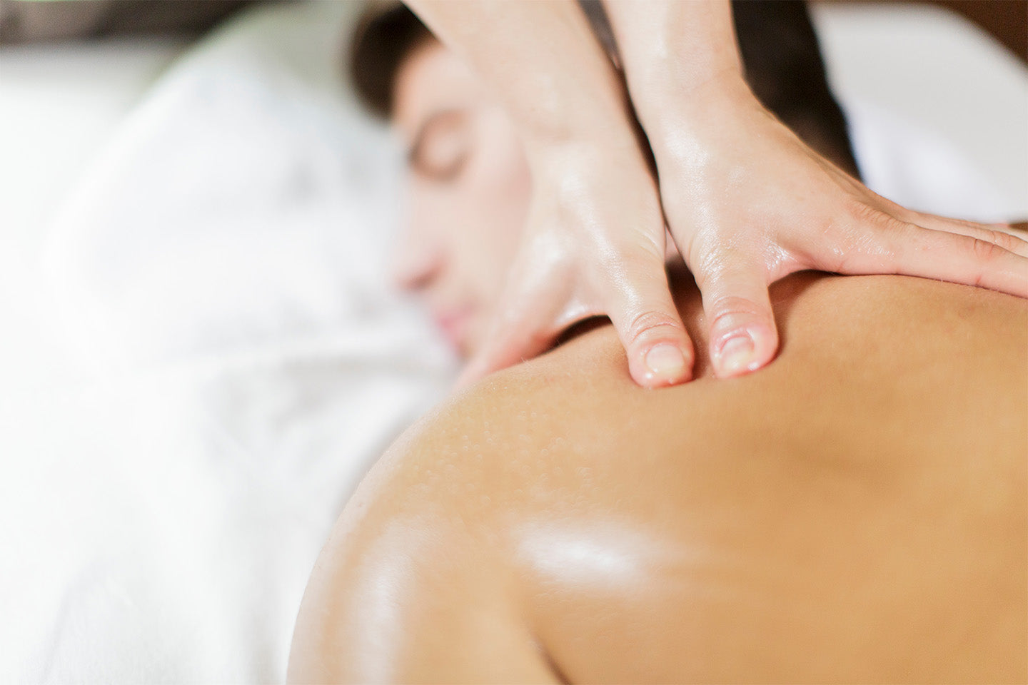 A close up shot of a relaxed man getting his shoulders massaged by a woman's hands.