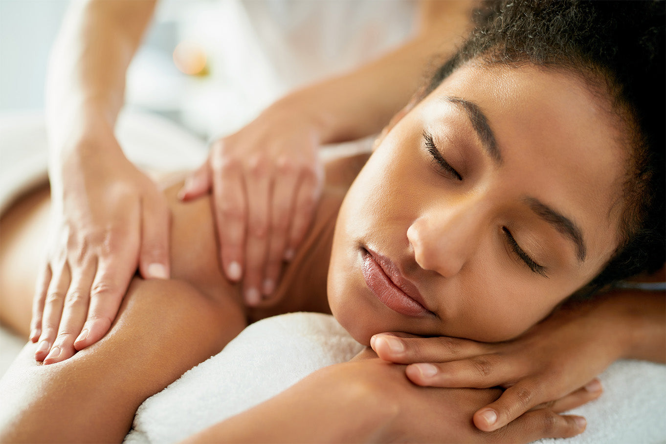A woman looking very serene and relaxed as she gets her shoulders massaged.