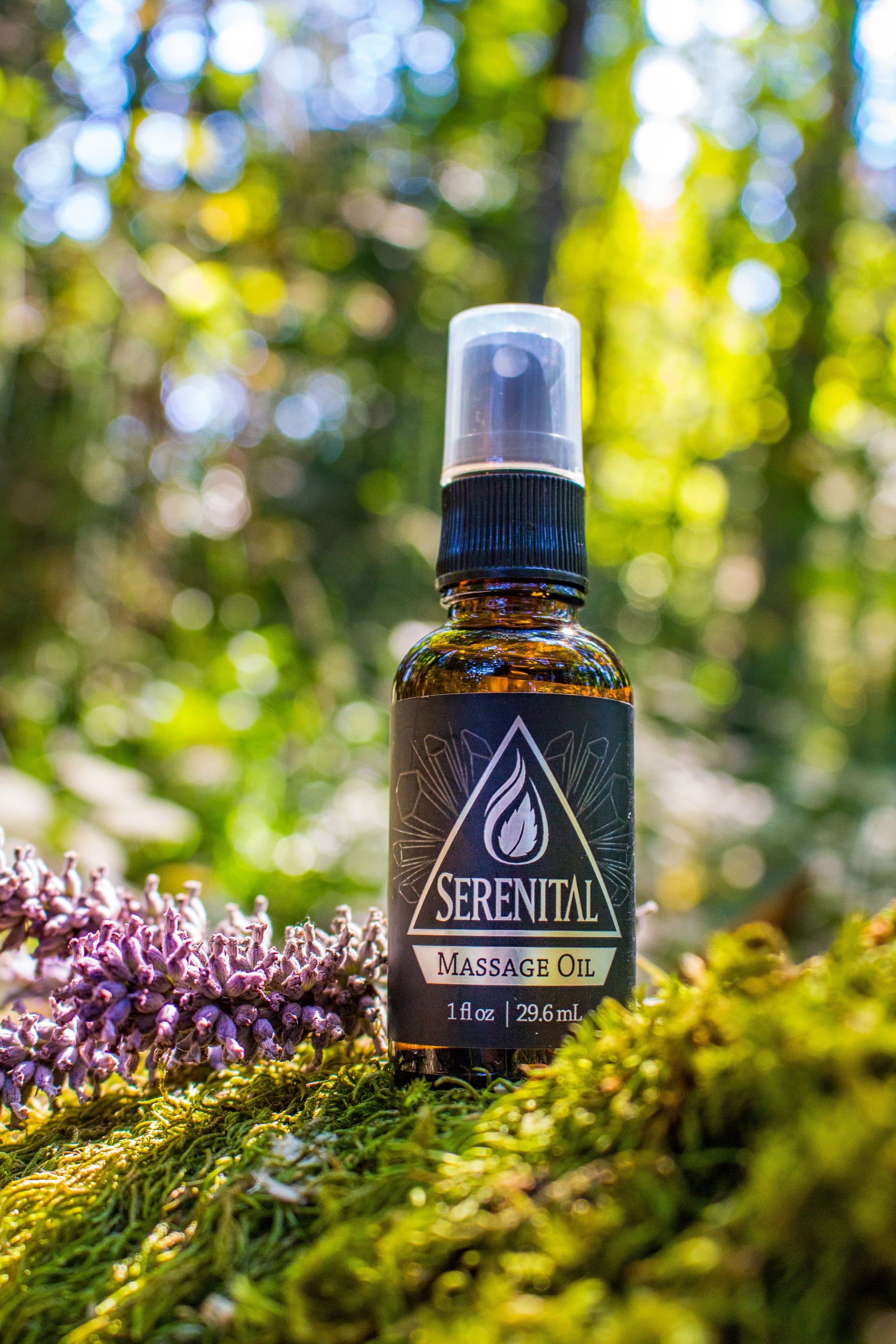 A bottle of Serenital CBD Massage Oil sits on a mossy log in the sunshine with a lavender bloom next to it.