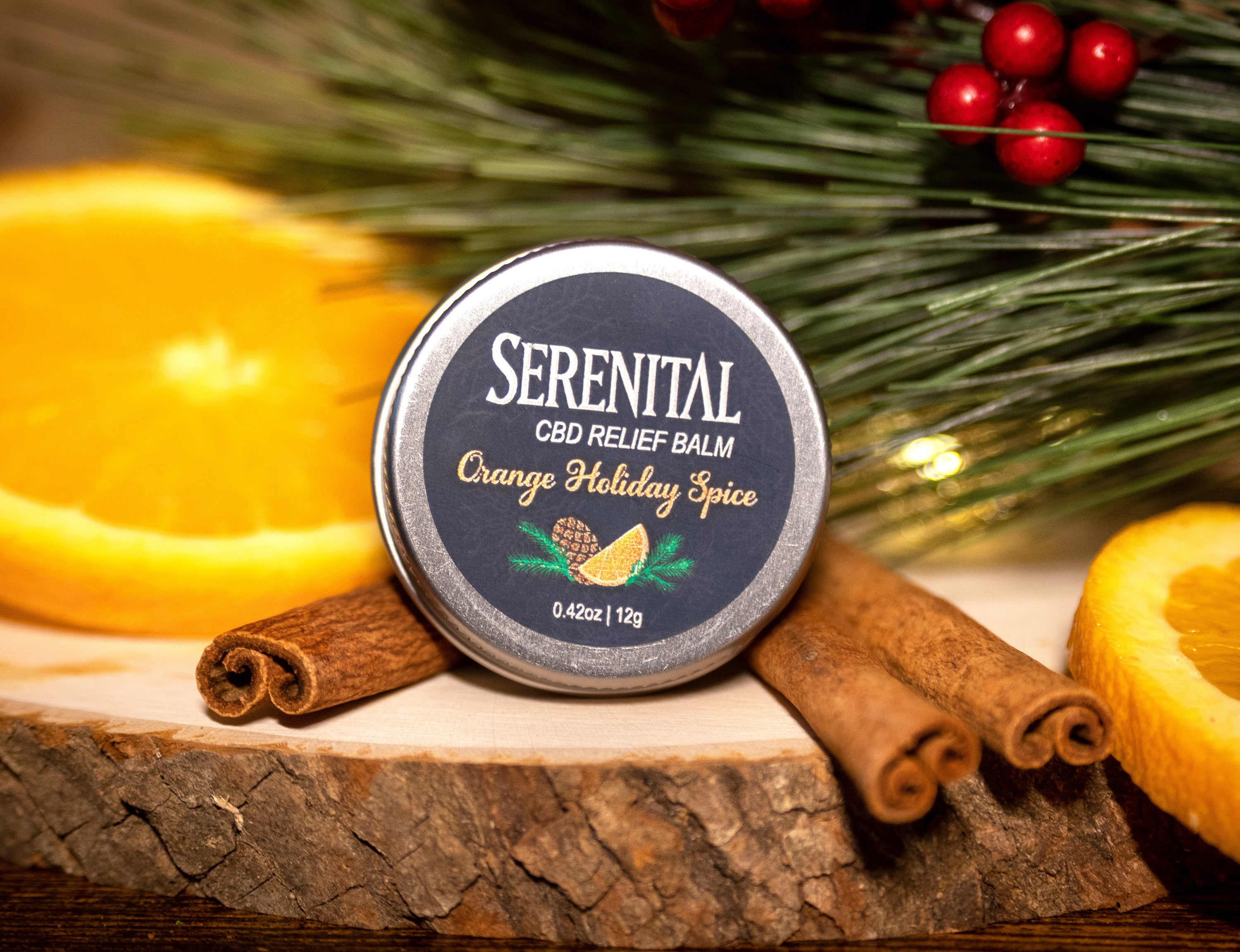 Serenital's limited release Orange Holiday Spice CBD relief balm is shown with some orange slices, cinnamon sticks, and pine needles.